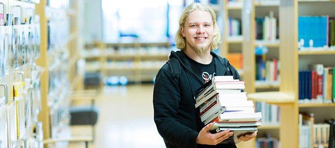 Opiskelija kantaa kirjapinoa Turun AMK:n kirjastossa