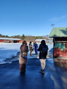 Toimittaja haastattelee ja kuvaa henkilöä. Kaksi opiskelijaa seuraa haastattelutilannetta talvisessa maisemassa.
