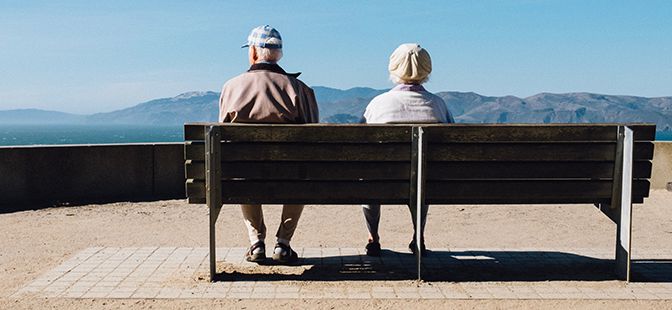Vanhan mies ja nainen istuvat penkillä katselemassa maisemaa.