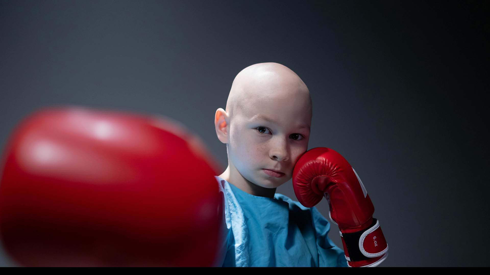Bald child looks at the camera, boxing gloves in hand