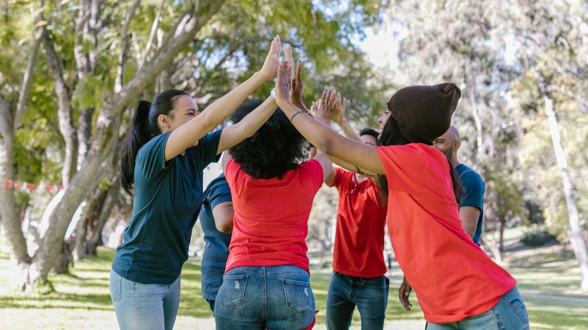 6 iloista nuorta ulkona ringissä kädet ylhäällä, taustalla näkyy isoja puita