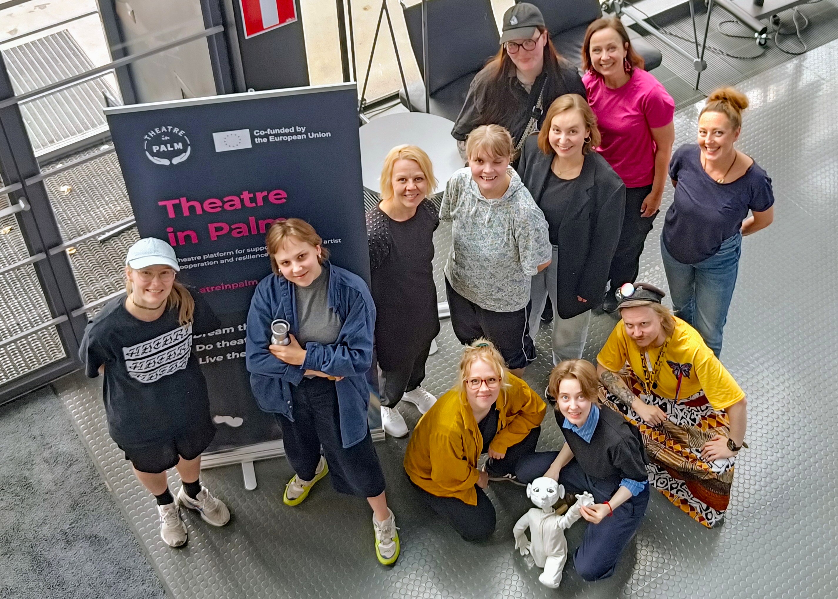 Iloisia ihmisiä yhmässä katsomassa ylöspäin, taustalla Theatre in Palm -roll-up