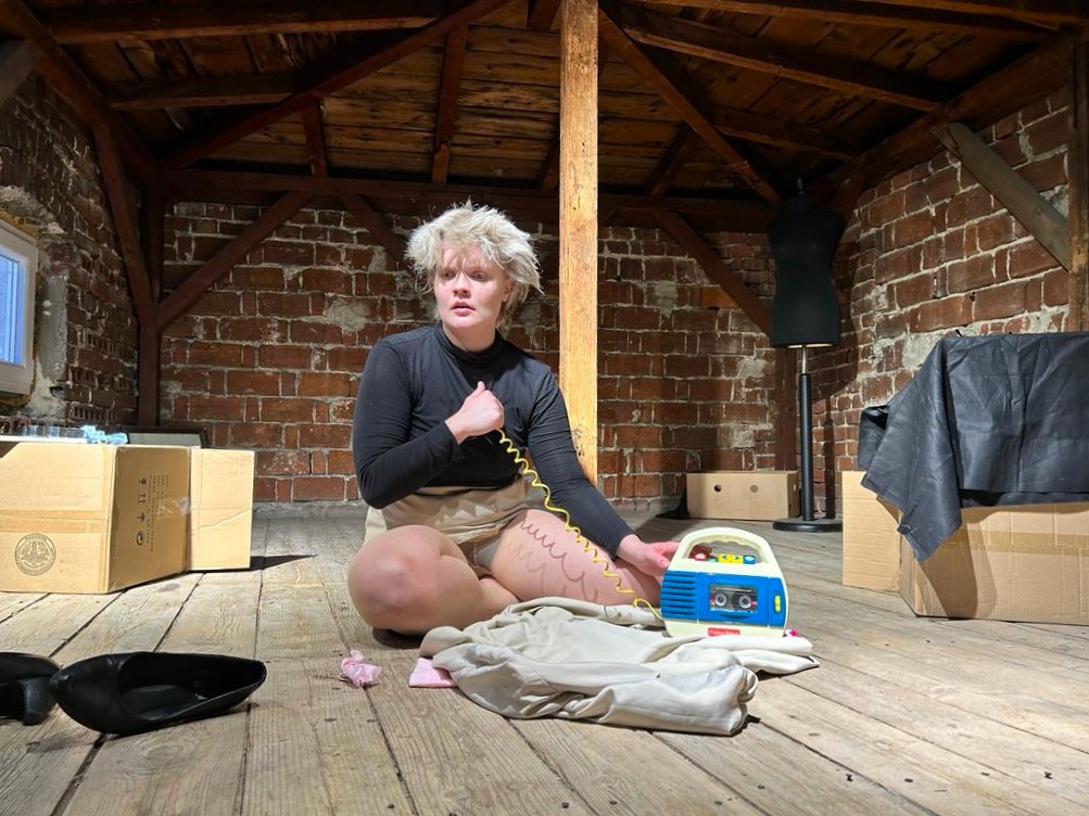 henkilö istuu puulattialla vintin näköisessä tilassa