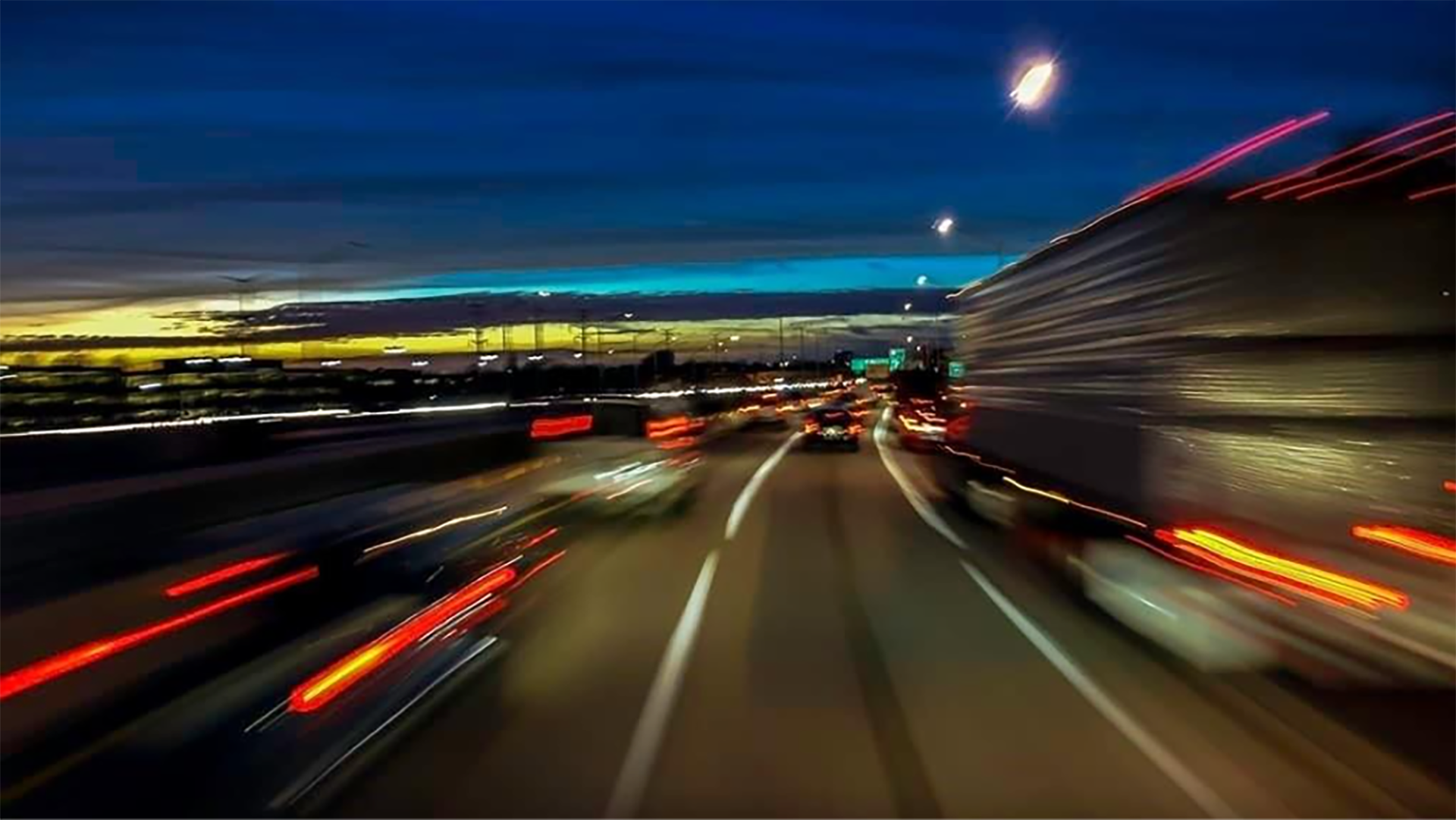 Pimeään aikaan otettu kuva monikaistaiselta vilkkaastiliikennöidyltä tieltä, oikealla erottu raskaanliikenteen ajoeuvo, muilla kaistoilla henkilöautoja