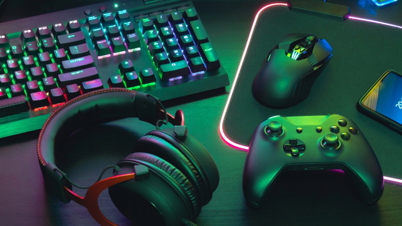 Näppäimistö, kuulokkeet, peliohjain, hiiri ja hiirimatto pöydällä.