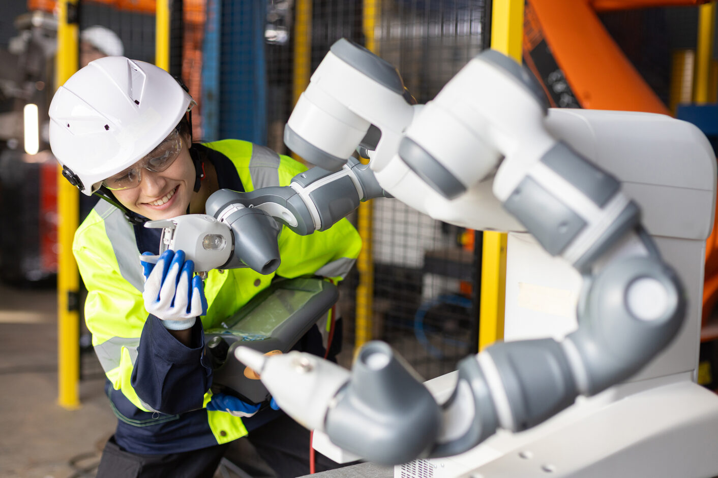 Female engineer operating collaborative robot in smart factory, smiling while adjusting robotic arm. Concept of cobot technology, automation, and human-robot interaction.