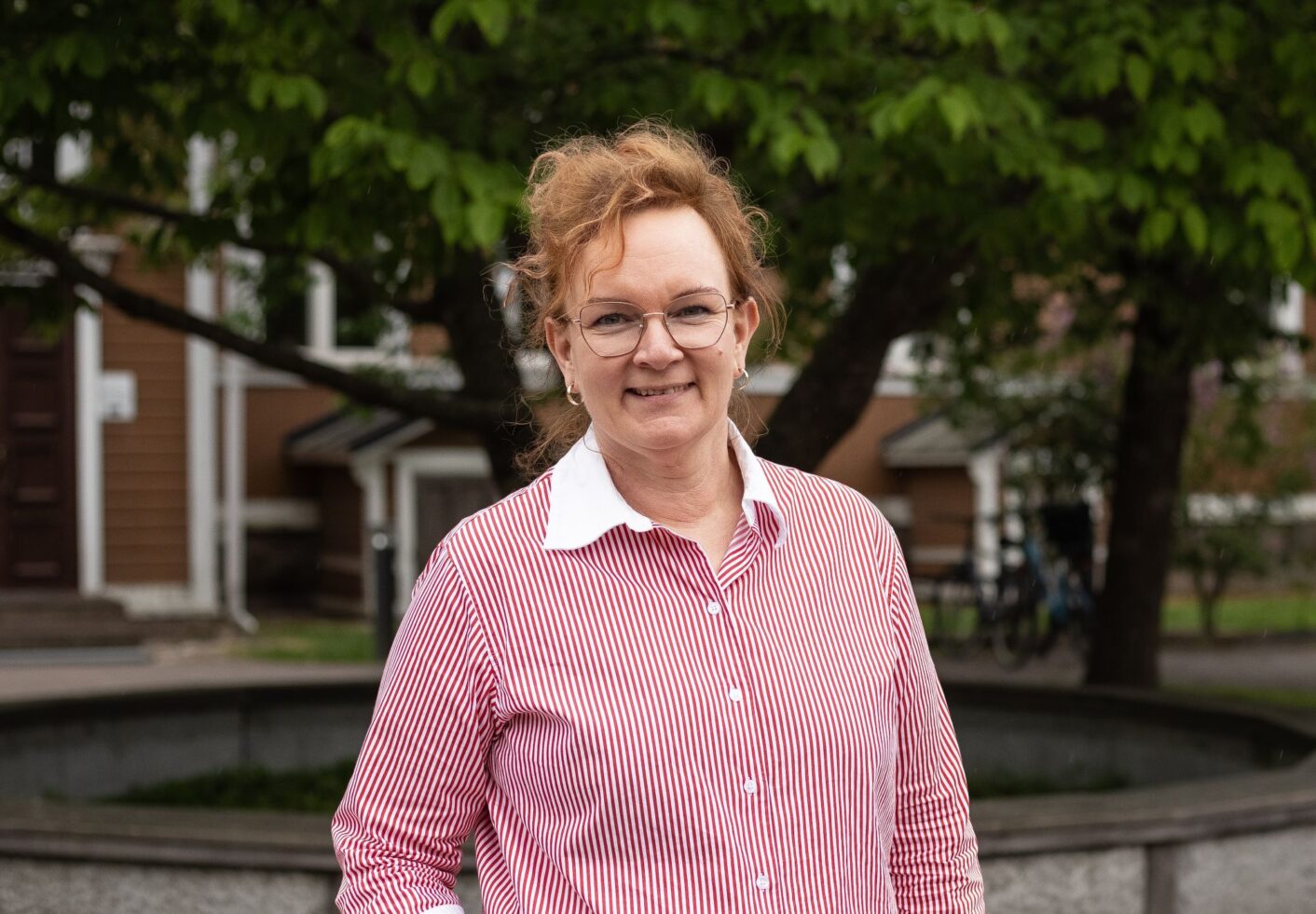 Minna Etelämäki, taustalla rakennus ja puiden lehvästöä