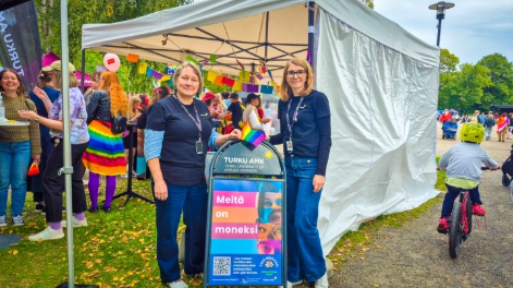 Turku AMK:n Satu Halonen ja Tiina Murto Turku Pride -tapahtumassa, välissä kyltti "Meitä on moneksi".