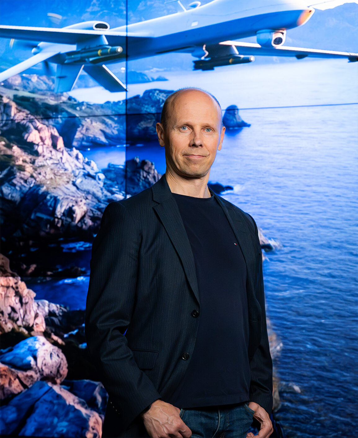 Henkilö seisoo sinisävyisen taustan edessä ja katsoo kameraan
